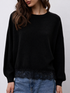 model wearing a black crew neckline knit with lace hem and blue jeans 