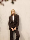 Woman wearing a brown suit against a plain background with woven belt
