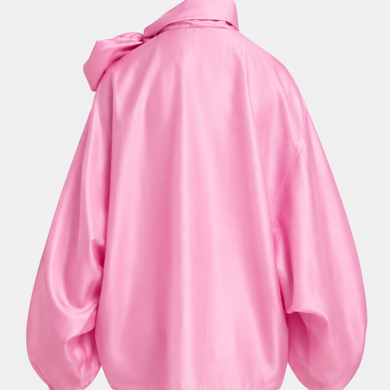 A pink satin blouse with a large bow at the high neck, balloon sleeves, and gathered cuffs, shown on a plain light gray background.