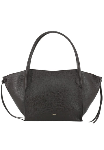 A brown pebbled leather handbag with a structured, asymmetrical silhouette, double top handles, and a small gold 'MNY' logo on the front, set against a plain white background.
