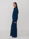 A model is shown in profile wearing a matching navy blue knit set consisting of a mock-neck long-sleeve top and wide-leg trousers, set against a plain light gray studio background.