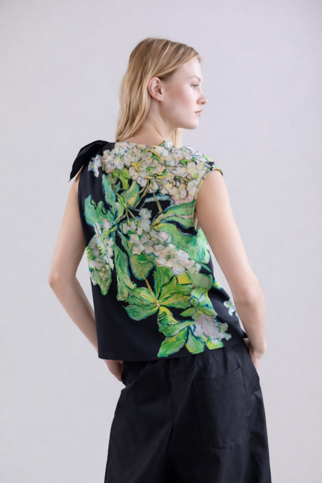 Woman wearing a silk sleeveless top with floral design on a plain background