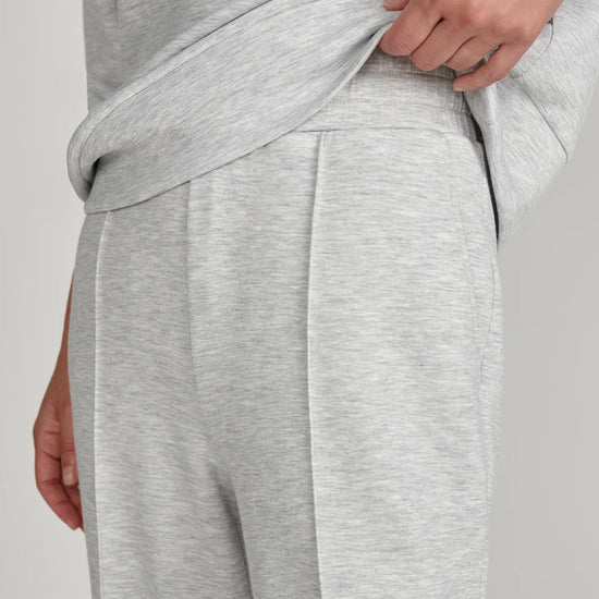 Close-up of a person wearing light heather gray lounge pants, pulling the waistband slightly upward with one hand.