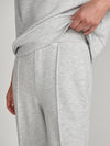 Close-up of a person wearing light heather gray lounge pants, pulling the waistband slightly upward with one hand.