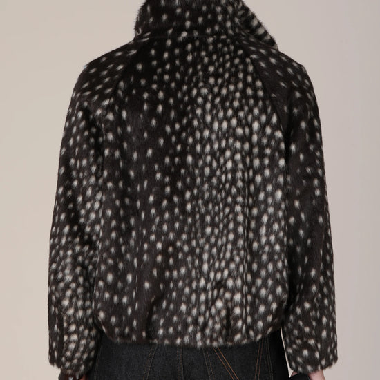 A person shown from the back wearing a dark cropped jacket with an allover light beige animal-like spot pattern, paired with dark jeans, against a plain light beige studio background.