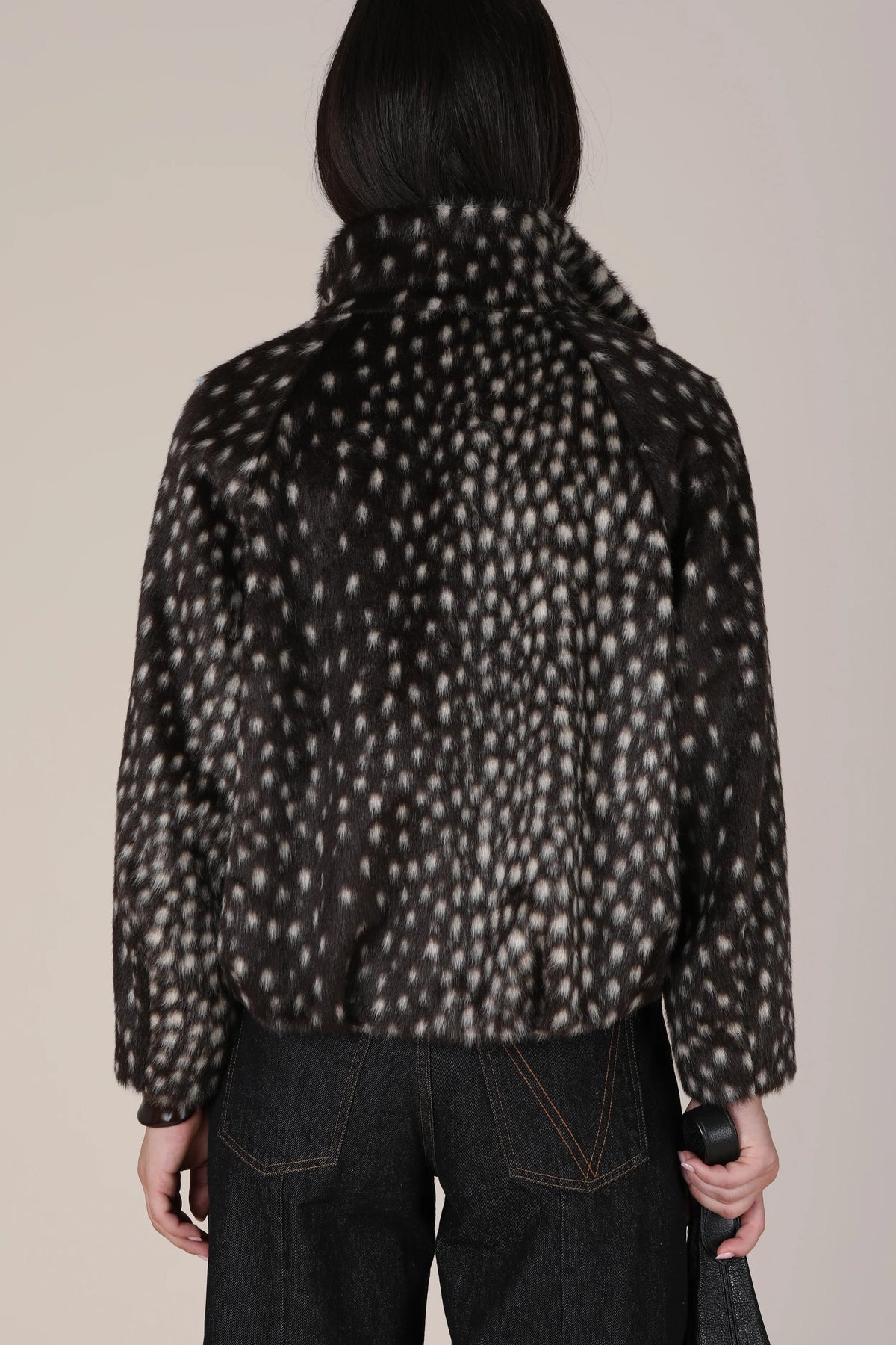 A person shown from the back wearing a dark cropped jacket with an allover light beige animal-like spot pattern, paired with dark jeans, against a plain light beige studio background.