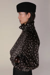 A side-profile view of a model wearing a black felt beret and a black faux-fur jacket with a white spotted pattern, set against a plain light beige background.