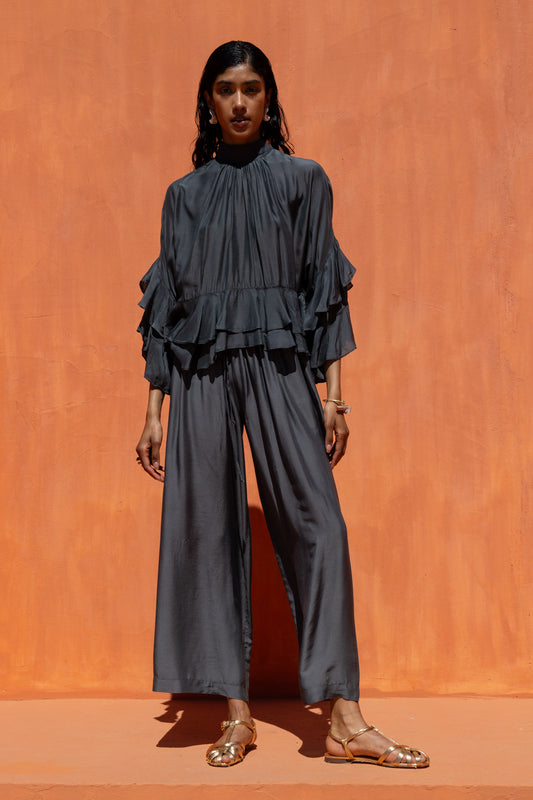 Woman wearing a dark gray layered top and wide-leg pants against an orange background