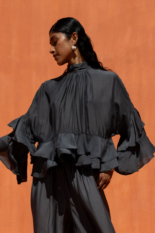 Woman wearing a black ruffled blouse against an orange background