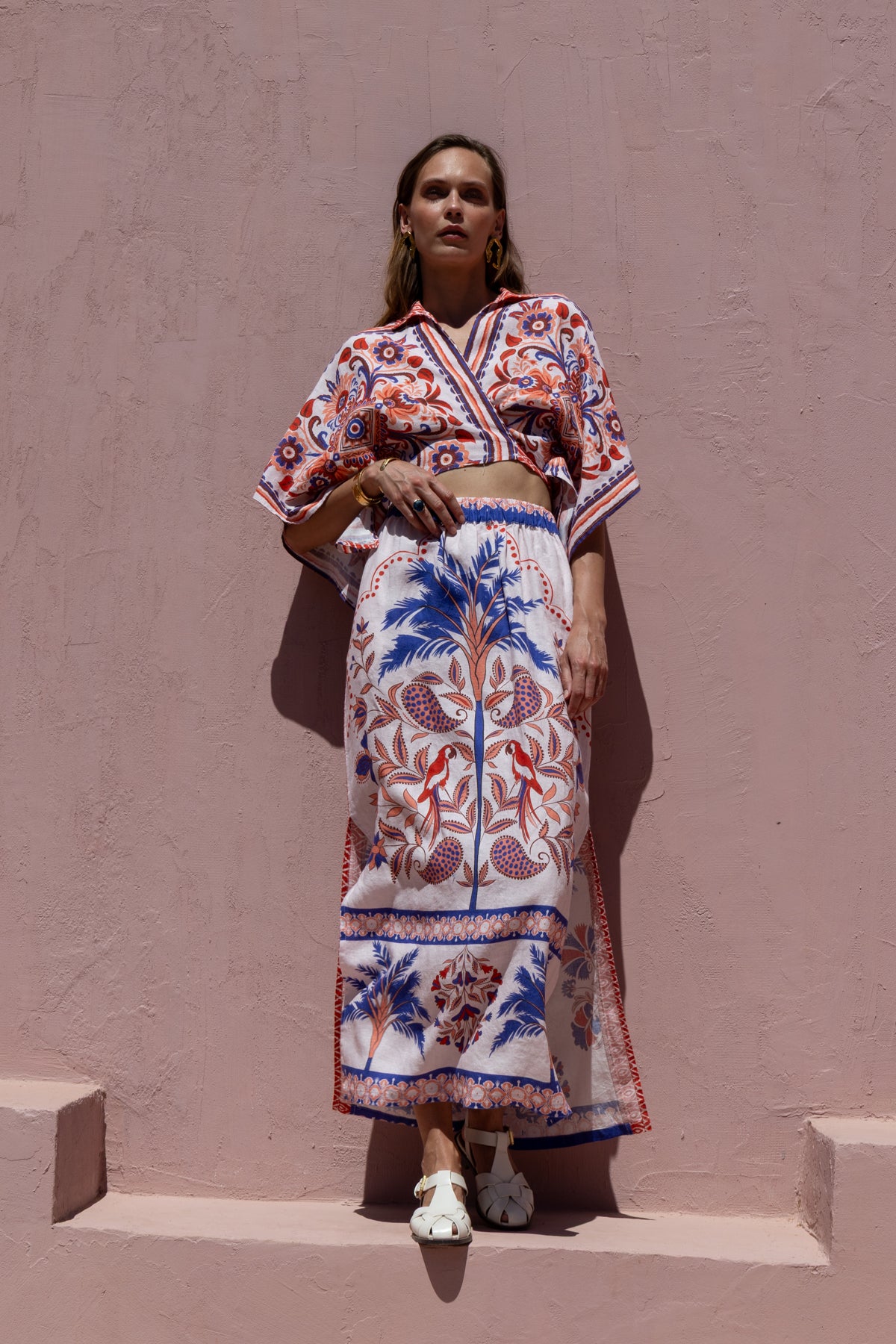 Woman wearing a colorful patterned outfit against a pink wall.