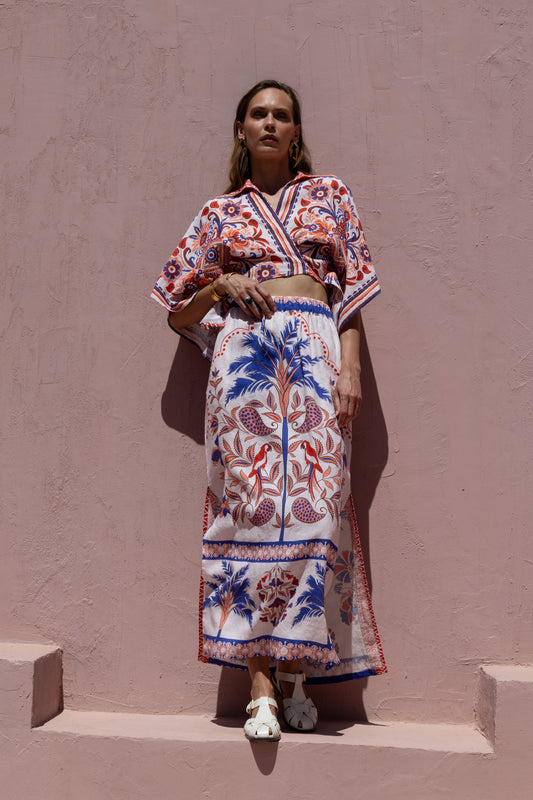 Woman wearing a colorful patterned outfit against a pink wall.