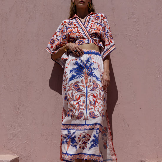 Woman wearing a colorful patterned outfit against a pink wall.