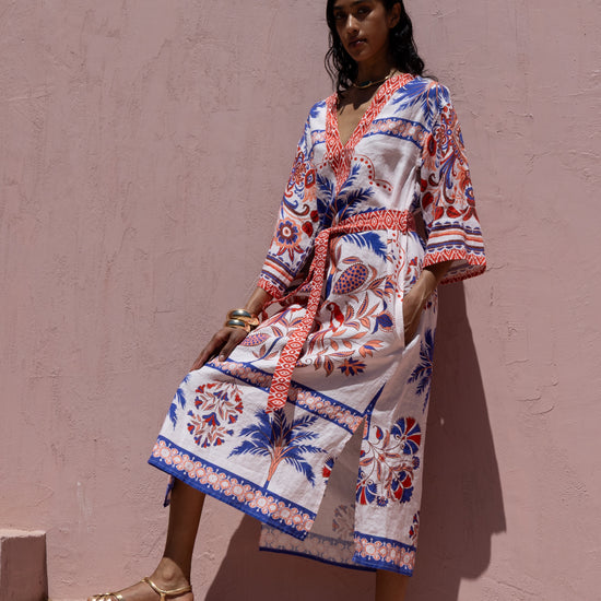 Woman wearing a colorful patterned dress against a pink wall
