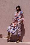 Woman wearing a colorful patterned dress against a pink wall