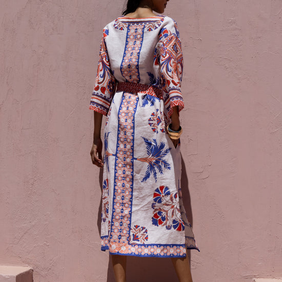 Woman wearing a patterned dress standing against a plain wall.
