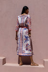Woman wearing a patterned dress standing against a plain wall.
