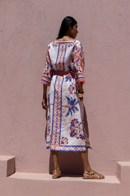 Woman wearing a patterned dress standing against a plain wall.