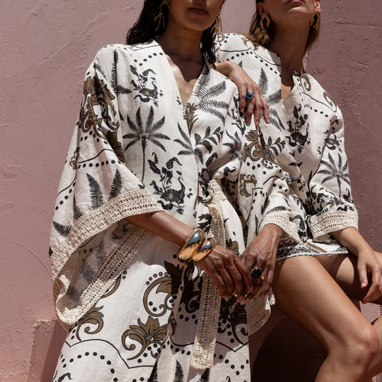Two women wearing patterned outfits against a pink wall.