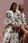 Two women wearing patterned outfits against a pink wall.
