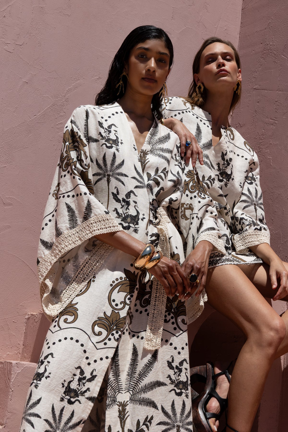 Two women wearing patterned outfits against a pink wall.