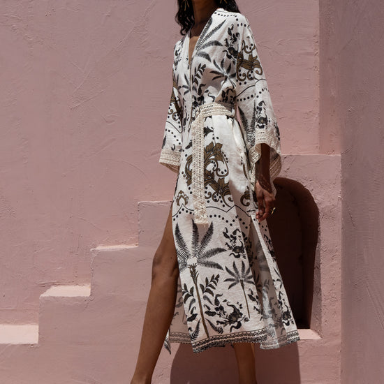 Woman wearing a white dress with black patterns against a pink wall.