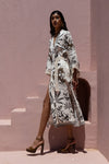 Woman wearing a white dress with black patterns against a pink wall.