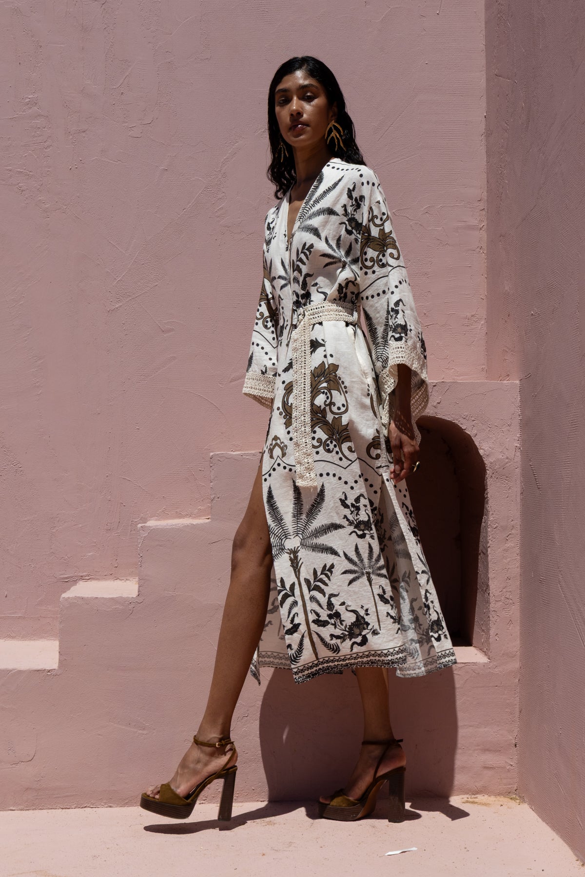 Woman wearing a white dress with black patterns against a pink wall.