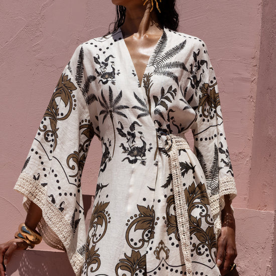 Woman wearing a white patterned dress against a pink wall