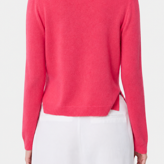 A model shown from the back wearing a bright pink knit sweater and white trousers against a plain light gray studio background.