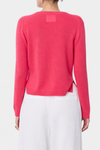 A model shown from the back wearing a bright pink knit sweater and white trousers against a plain light gray studio background.