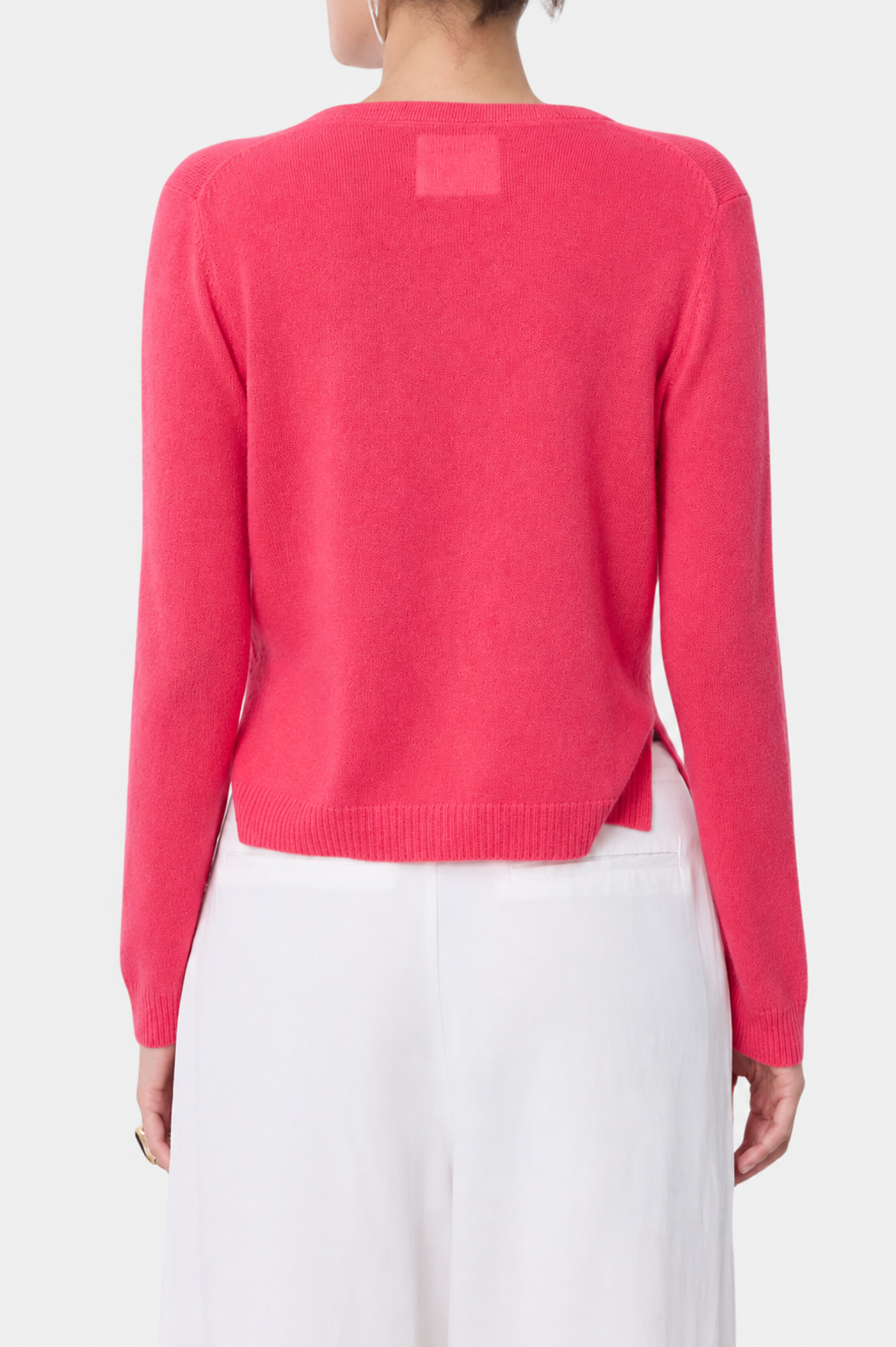 A model shown from the back wearing a bright pink knit sweater and white trousers against a plain light gray studio background.