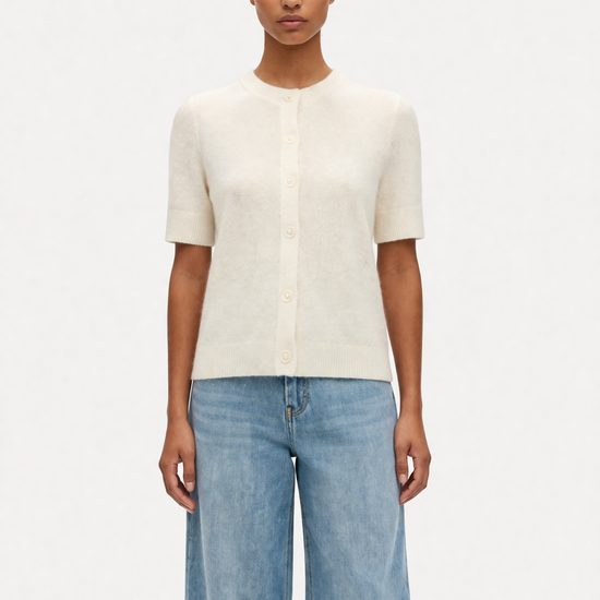 model wearing cream jumper and jeans on plain background