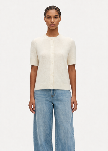 model wearing cream jumper and jeans on plain background