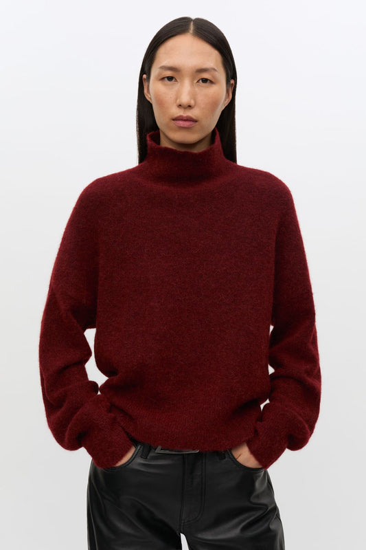 Model in turtleneck jumper in deep red worn with leather trousers