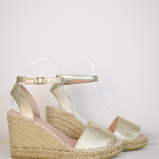 A gold wedge sandal with open toes and an ankle strap 