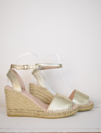 A gold wedge sandal with open toes and an ankle strap 