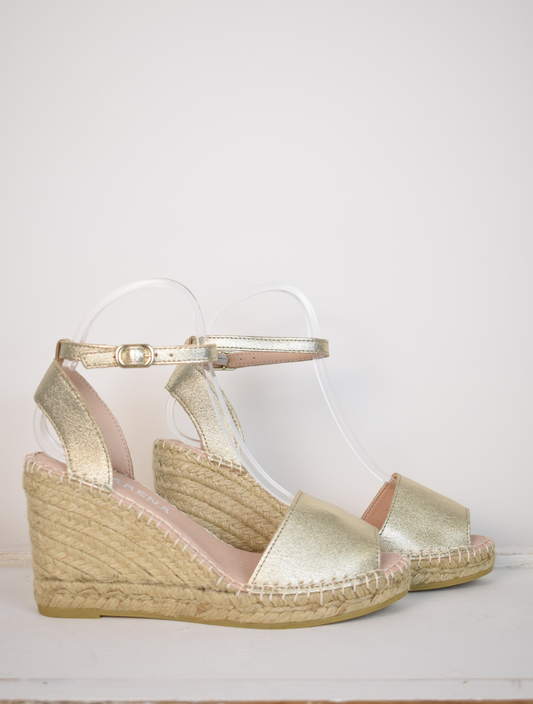 A gold wedge sandal with open toes and an ankle strap 