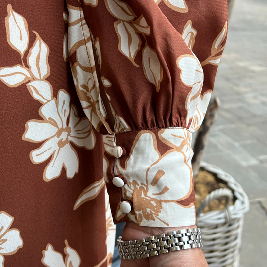 A long vintage style dress with a tan background and a white floral print 