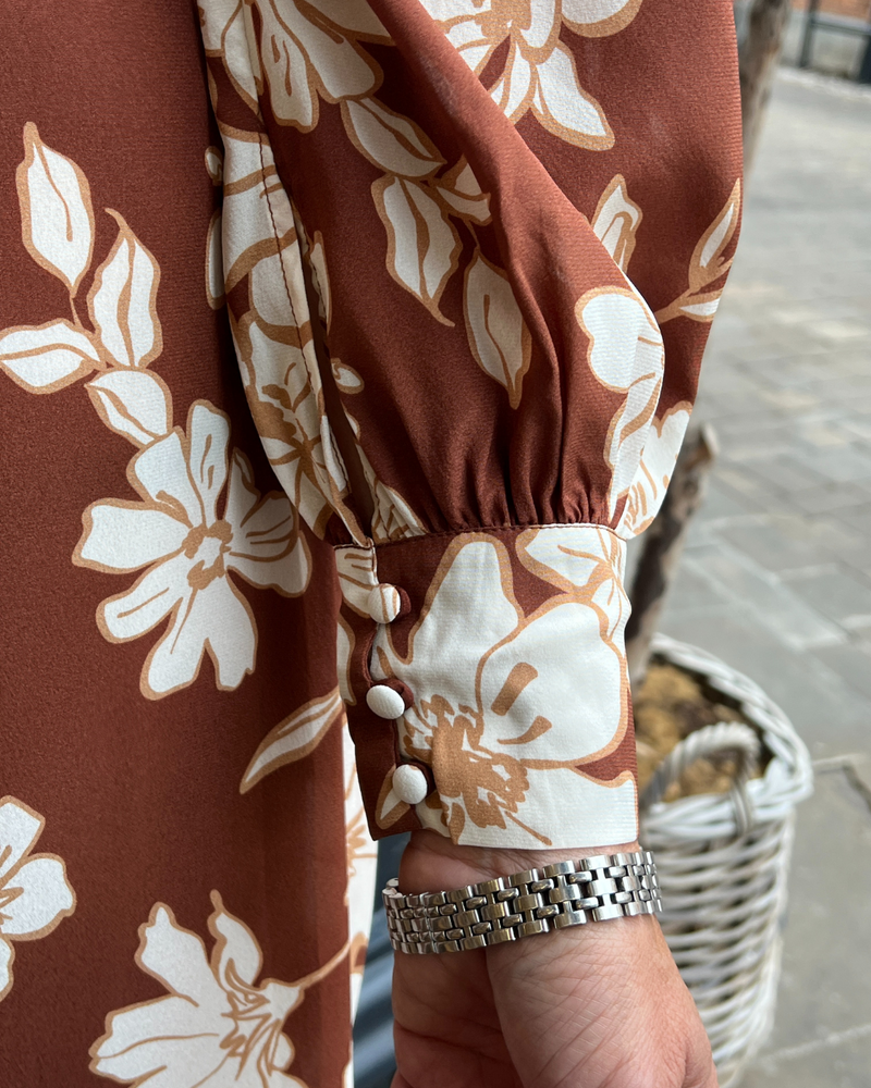 A long vintage style dress with a tan background and a white floral print 