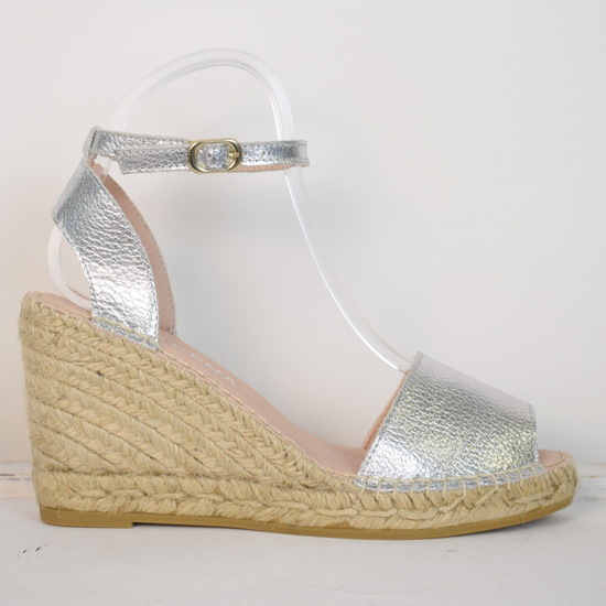 A silver wedge sandal with open toes and an ankle strap 