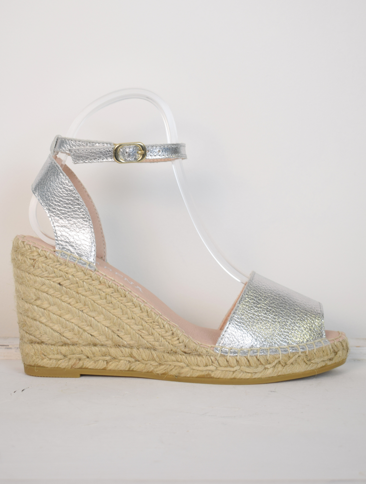 A silver wedge sandal with open toes and an ankle strap 