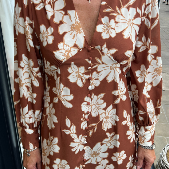 A long vintage style dress with a tan background and a white floral print 