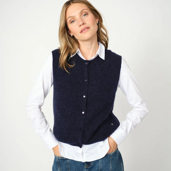 woman wearing a blue knit vest over a white shirt and blue jeans 