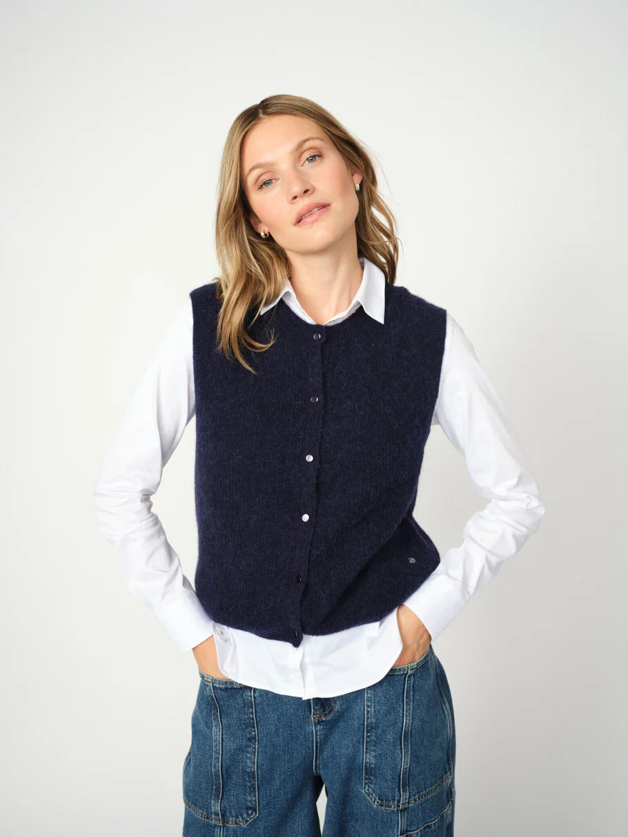 woman wearing a blue knit vest over a white shirt and blue jeans 