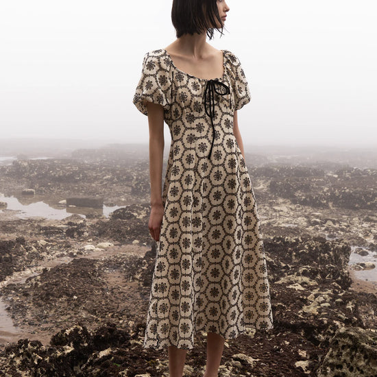 Woman in a patterned dress standing on a mountain with a scenic view in the background