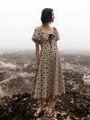 Woman in a patterned dress standing on a mountain with a scenic view in the background