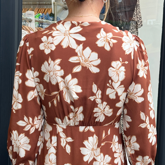 A long vintage style dress with a tan background and a white floral print 