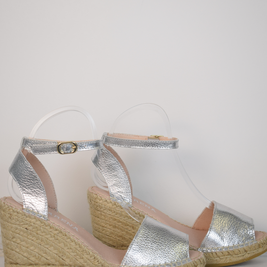 A silver wedge sandal with open toes and an ankle strap 