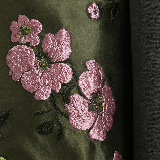 Close-up of a dark olive green fabric with pink floral embroidery and green leaves, next to a dark gray fabric.