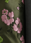 Close-up of a dark olive green fabric with pink floral embroidery and green leaves, next to a dark gray fabric.